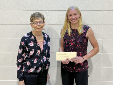 Two people posing in front of a white painted concrete brick wall. On the left is Kathleen O'Hearn of the Friends of the Library. On the right is Carlee Zimmermann of Lakeside Lutheran High School who was awarded the 2023 Friends Scholarship for $1,500.